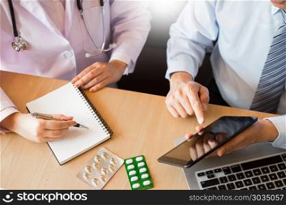 Two doctors discussing patient notes in an office pointing to tablet as they make a diagnosis or decide on treatment.. Two doctors discussing patient notes in an office pointing to a