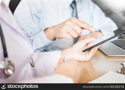 Two doctors discussing patient notes in an office pointing to tablet as they make a diagnosis or decide on treatment.. Two doctors discussing patient notes in an office pointing to a