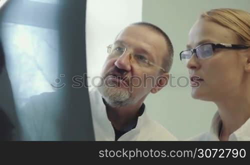 Two doctors, young and mature, are looking over patient&acute;s X-ray pictures and discussing them.