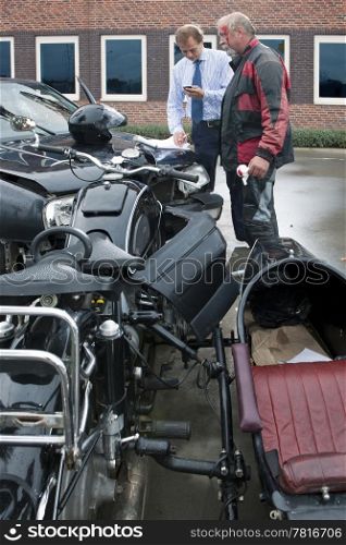 two drivers exchanging information for insurance purposes after a car crash involving a car and a classic sidecar motorcycle