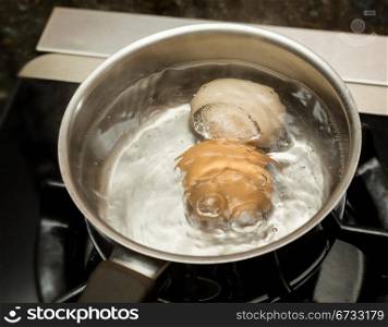 Two eggs in boiling water in stainless steel pan on gas hob