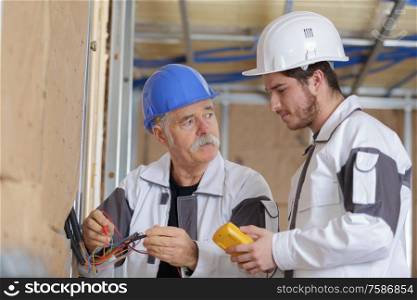two electrician checking socket voltage with digital multimeter