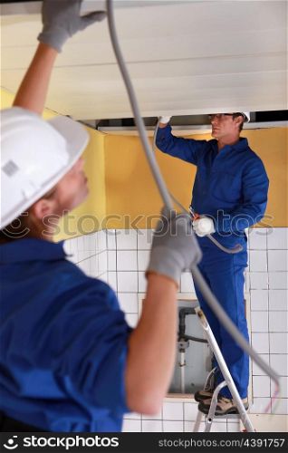 Two electrician feeding length of cable through ceiling