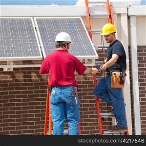 Two electricians installing solar panels on the side of a building.