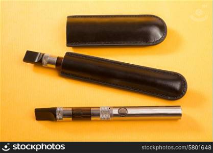 Two electronic cigarettes lie on a yellow background, with one unit still in leather pouch.