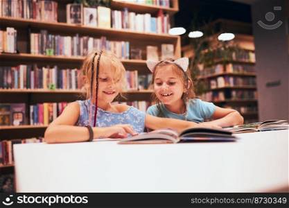 Two elementary schoolgirls doing homework in school library. Students learning from books. Pupils having fun in library. Back to school