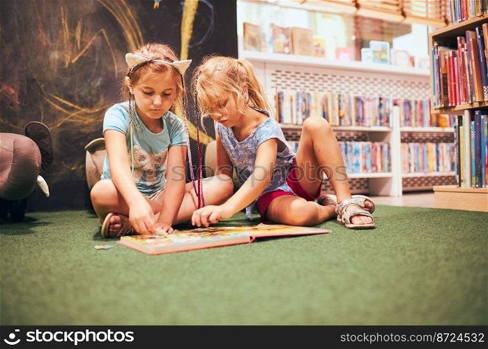 Two elementary schoolgirls solving puzzles and riddles in school library. Students learning from books. Pupils having fun in library. Back to school