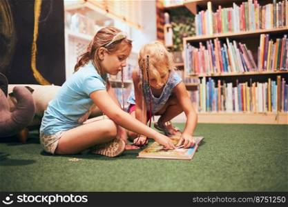 Two elementary schoolgirls solving puzzles and riddles in school library. Students learning from books. Pupils having fun in library. Back to school