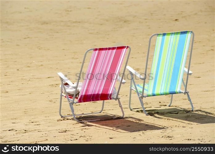 Two empty colorful beach chairs on a sandy beach