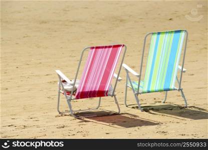 Two empty colorful beach chairs on a sandy beach