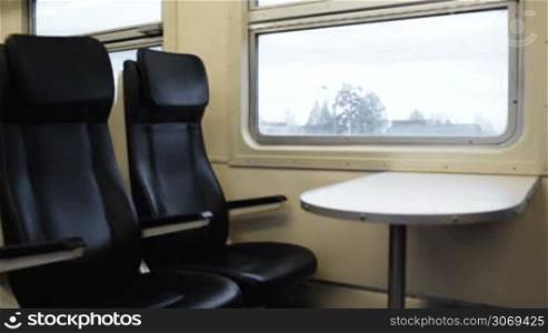 Two empty comfortable black seats with table in front of them in the train moving slowly