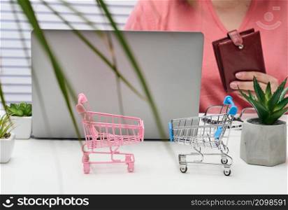 two empty miniature carts, an open laptop and a woman with a purse sitting at a white table. Online shopping, sale