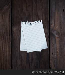 two empty notepad paper attached with a button on a brown wooden surface