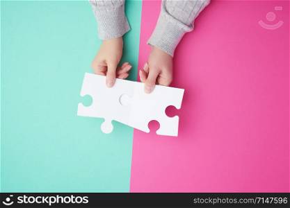 two empty paper white pieces of puzzles in female hands, puzzle connected, colorful background, top view