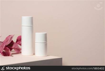 two empty white plastic tubes for cosmetics stands on a wooden podium on a beige background with a shadow. Containers for cream, shampoos, liquid substances. Branding, template