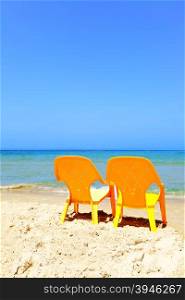 Two empty yellow chairs on beach close up