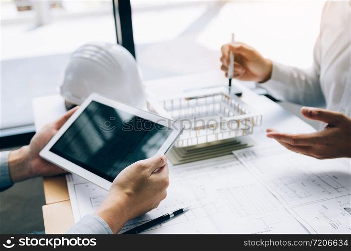 Two engineering working together and using digital tablet looking blueprint and analysis with architectural plan on desk.