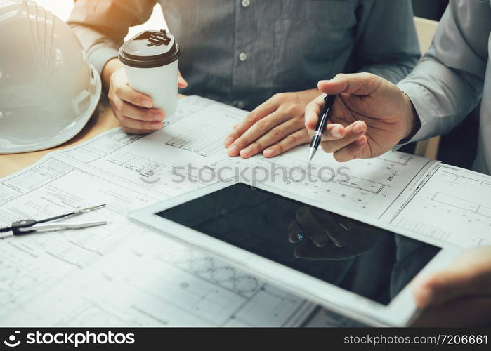 Two engineering working together and using digital tablet looking blueprint and analysis with architectural plan on desk.