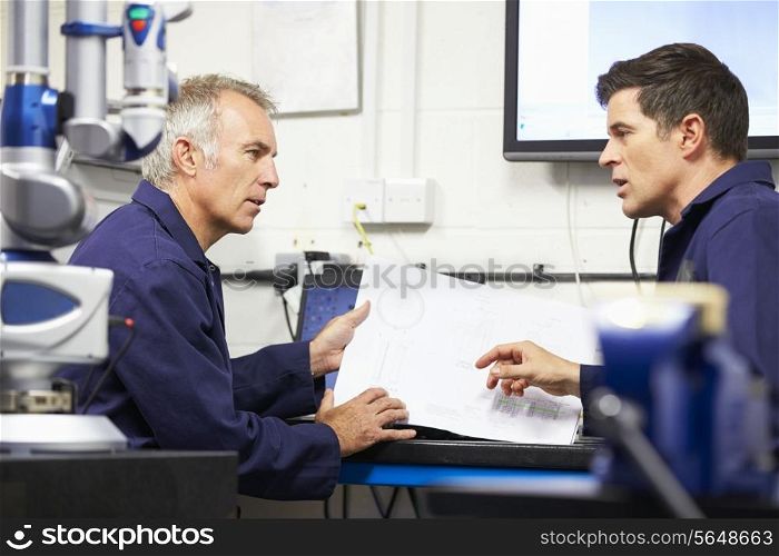 Two Engineers Discussing Plans With CMM Arm In Foreground