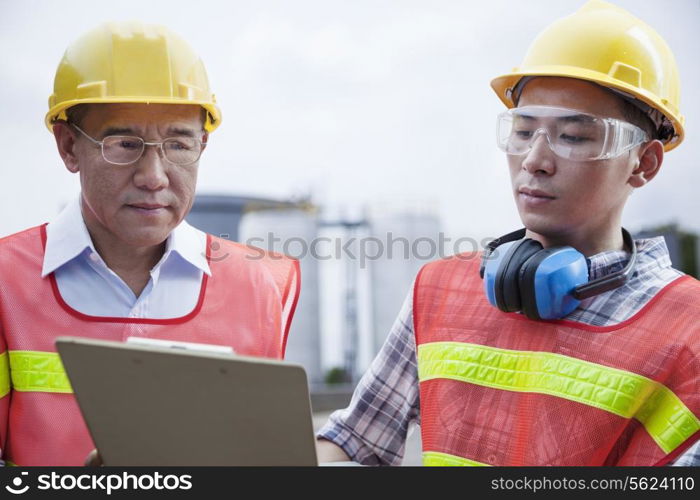 Two engineers in protective workwear looking down at a clipboard outside of a factory