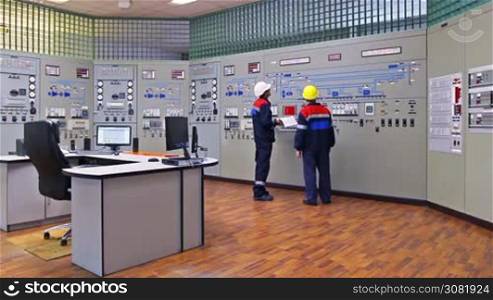 two engineers talk while showing examples on circuit at main control panel of gas compressor station