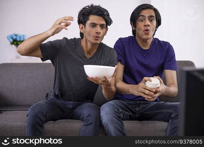 Two excited teenage boys gesturing while watching TV in living room