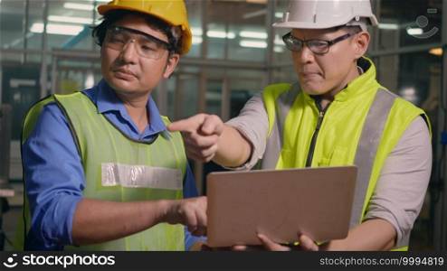 Two factory industrial workers technician or engineer and manager wear uniforms safety feeling upset with the engine machine of the factory arguing about planning procedure of work on laptop computer