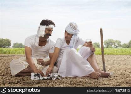 Two farmers sitting in field drinking tea and eating snacks