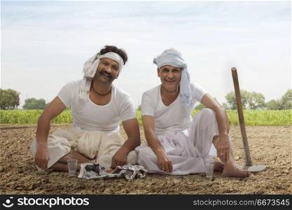 Two farmers sitting in field drinking tea and eating snacks