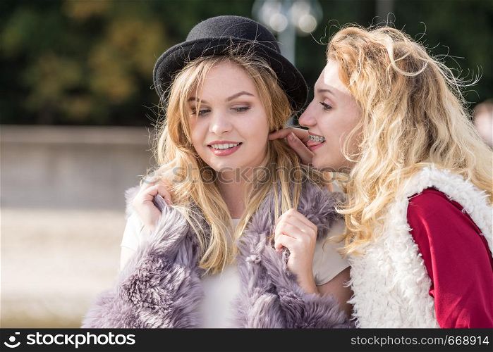 Two fashionable women wearing stylish outfits during warm autumnal weather gossiping together.. Two fashionable women gossiping
