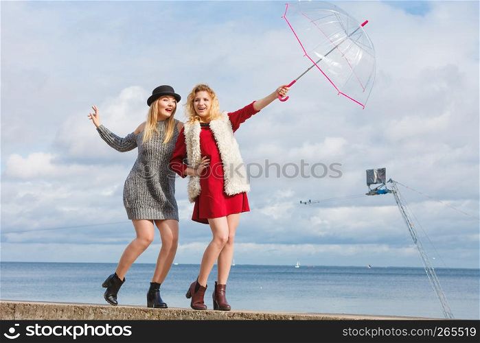 Two fashionable women wearing stylish outfits holding transparent umbrella spending their free time outdoor. Two fashionable women and umbrella