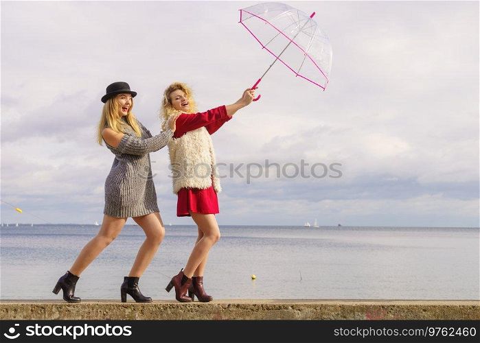Two fashionable women wearing stylish outfits holding transparent umbrella spending their free time outdoor. Two fashionable women and umbrella