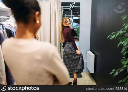 Two female customers choosing clothes in the dressing room, shopping. Shopaholics in clothing store, purchasing, fashion
