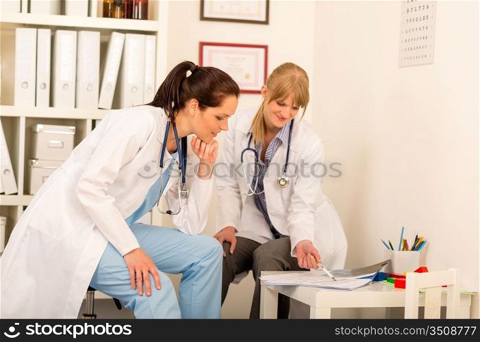 Two female doctors discuss documents at medical office together