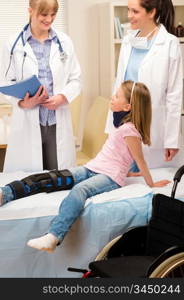 Two female doctors examine broken leg little girl wheelchair