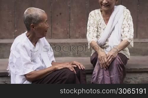 Two female friends and senior asian women sitting against brown wall during friendly conversation
