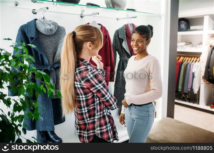Two female friends choosing coats in shop, shopping. Shopaholics in clothing store, consumerism lifestyle. Two female friends choosing coat in shop, shopping