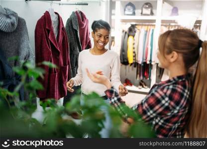 Two female friends choosing coats in shop, shopping. Shopaholics in clothing store, consumerism lifestyle, fashion