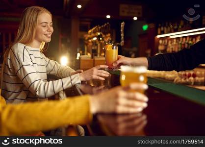 Two female friends drinks alcohol at the counter in bar. Group of people relax in pub, night lifestyle, friendship, event celebration. Female friends drinks alcohol at counter in bar