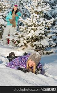 Two female friends enjoy winter countryside laughing lying in snow