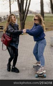 two female friends having fun skateboarding outdoors