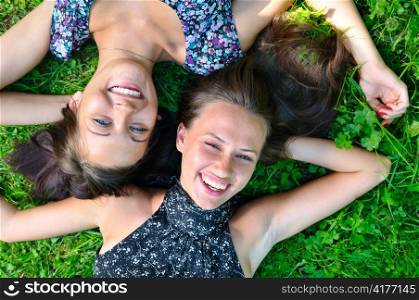 two female friends is lying on grass and laughing