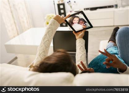 Two female friends making a selfie with a digital tablet sitting on the couch at home. Multiethnic women.. Two female friends making a selfie with a digital tablet sitting on the couch at home.