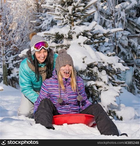 Two female friends on bobsleigh winter snow laughing having fun