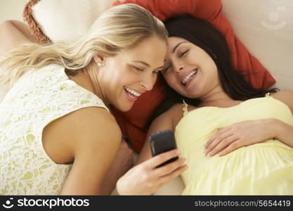 Two female Friends On Sofa Reading Text Message