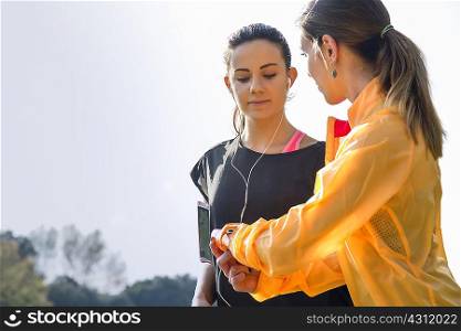 Two female friends outdoors, young woman showing friend activity tracker