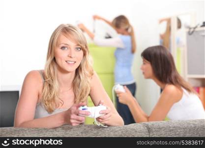 Two female friends playing video games with other friend in background