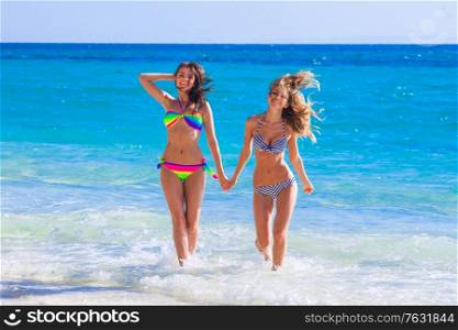 Two female friends run from sea waves to beach holding hands and laughing. Two female friends run to beach