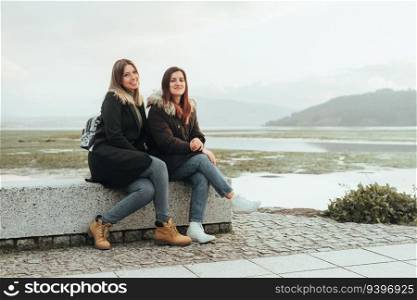 Two female friends sitting on a bench against a sw&landscape