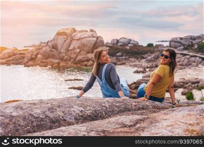 Two female friends sitting on a rock at sunset